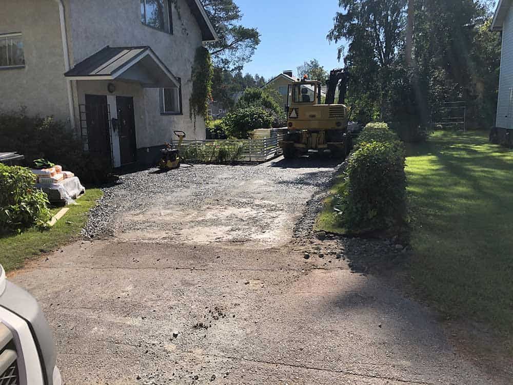 Ajotie rakenteilla. Keltainen työmaa-auto, soraa, talo taustalla.