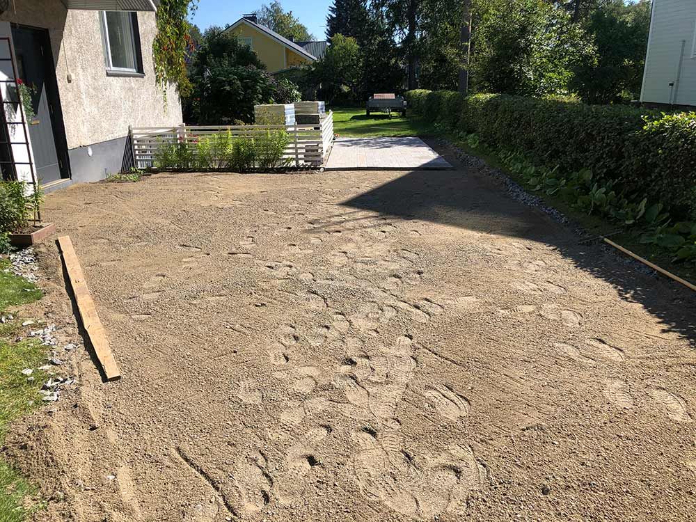Hiekkatie, jonka vasemmalla puolella on talo ja oikealla vehreyttä, valmiina päällystykseen.