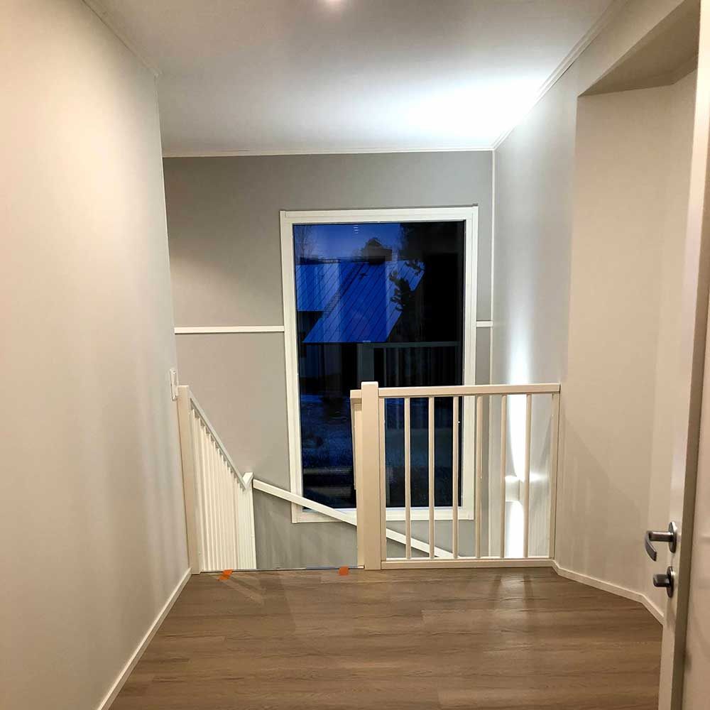 Käytävä, jossa on portaikko ja suuri ikkuna, puulattia ja neutraalin sävyiset seinät.