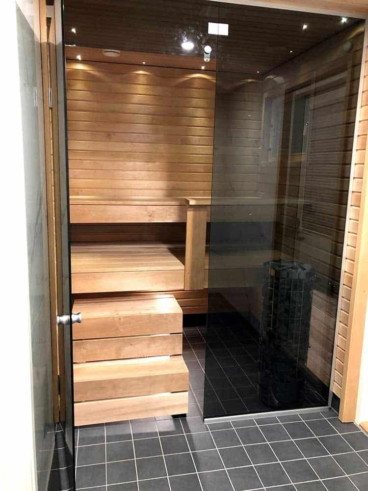 Saunassa puiset penkit, lasiovi ja laattalattia.