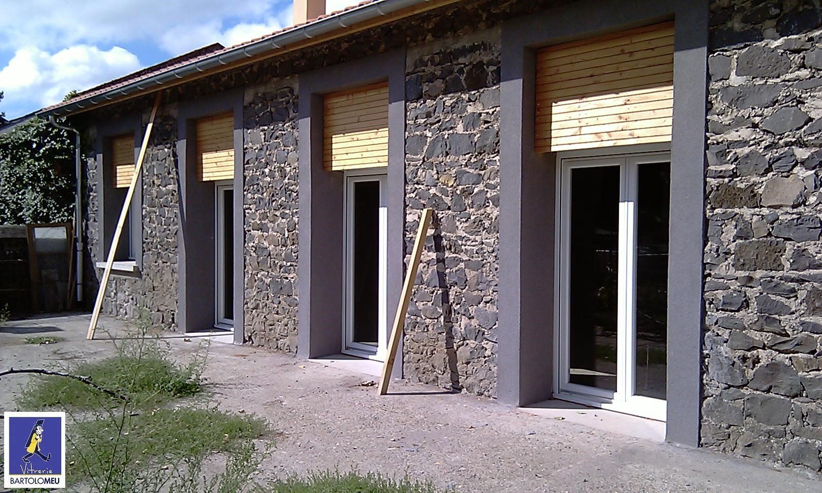 Façade de maison en pierre avec menuiseries blanches et volets en bois