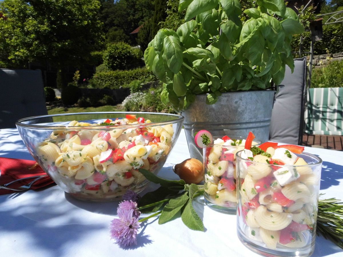 eine Schüssel Nudelsalat steht auf einem Tisch neben zwei Gläsern