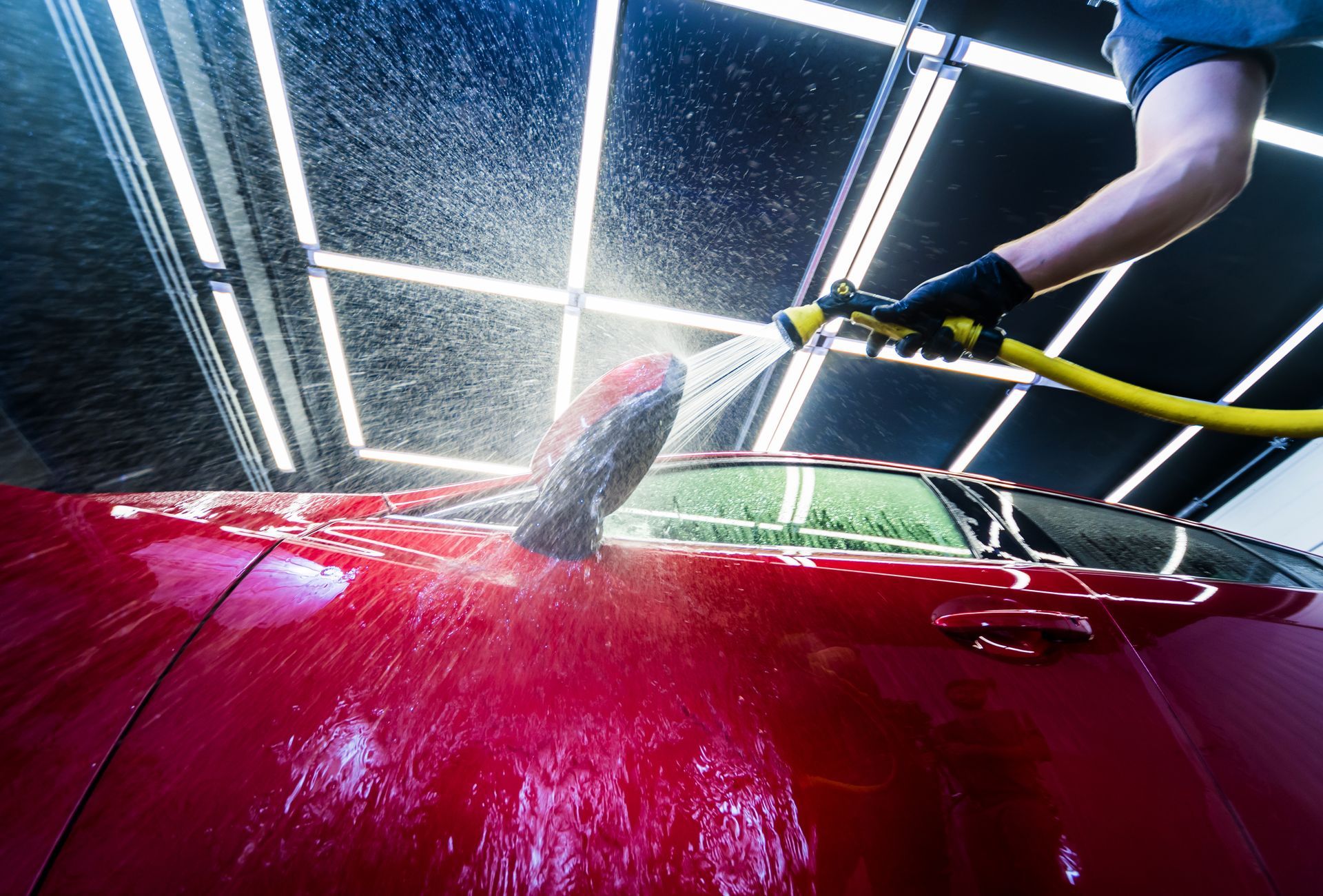 Persona lavando un coche rojo brillante con una manguera.
