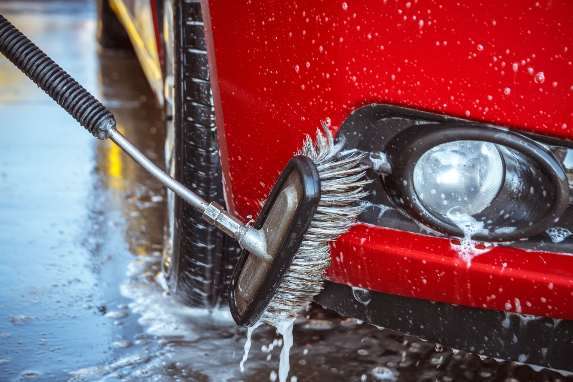 Un coche rojo se lava con un cepillo de mango largo en un lavadero de coches; se ve espuma.
