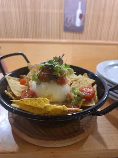 Nachos con aderezos en una sartén negra sobre un posavasos de madera. Incluye totopos, salsa y queso blanco.