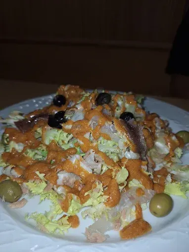 Ensalada con lechuga, aceitunas, anchoas y salsa de naranja en un plato blanco.