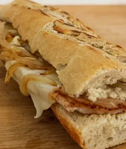 Sándwich submarino con queso derretido, cebollas caramelizadas y carne sobre una superficie de madera.