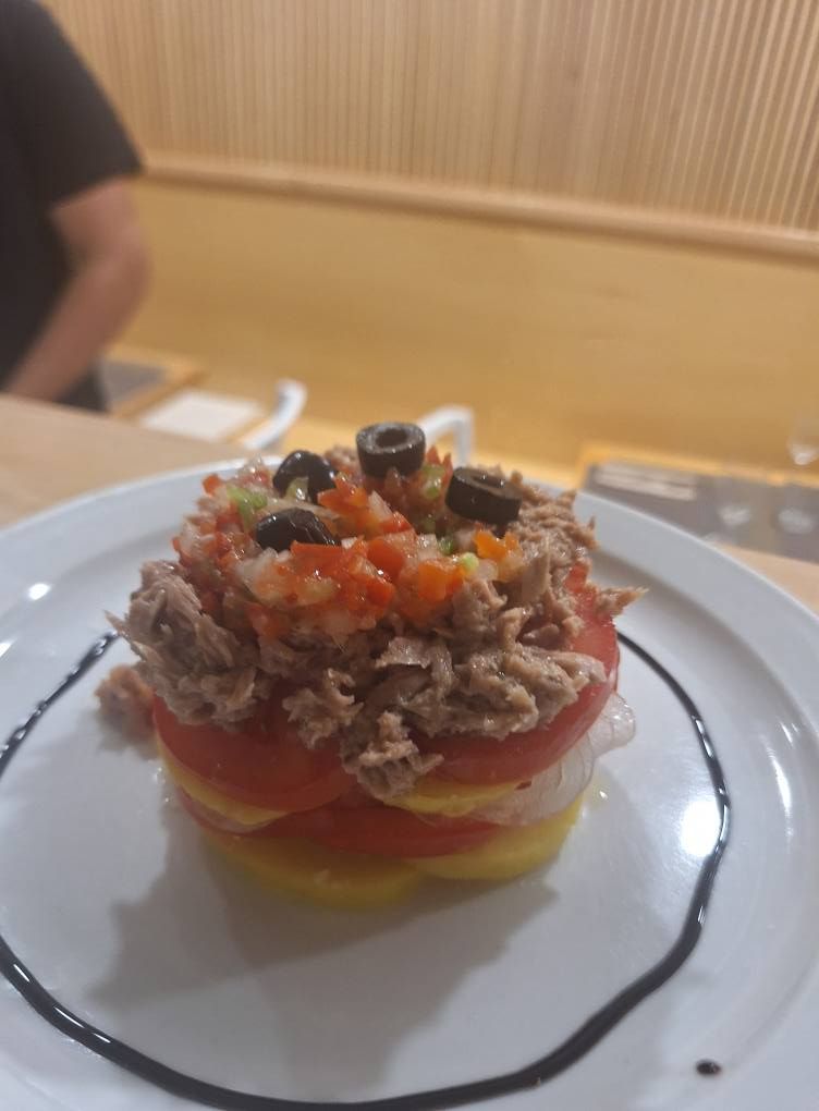 Ensalada de tomate y atún apilados con aceitunas y glaseado balsámico en un plato blanco.