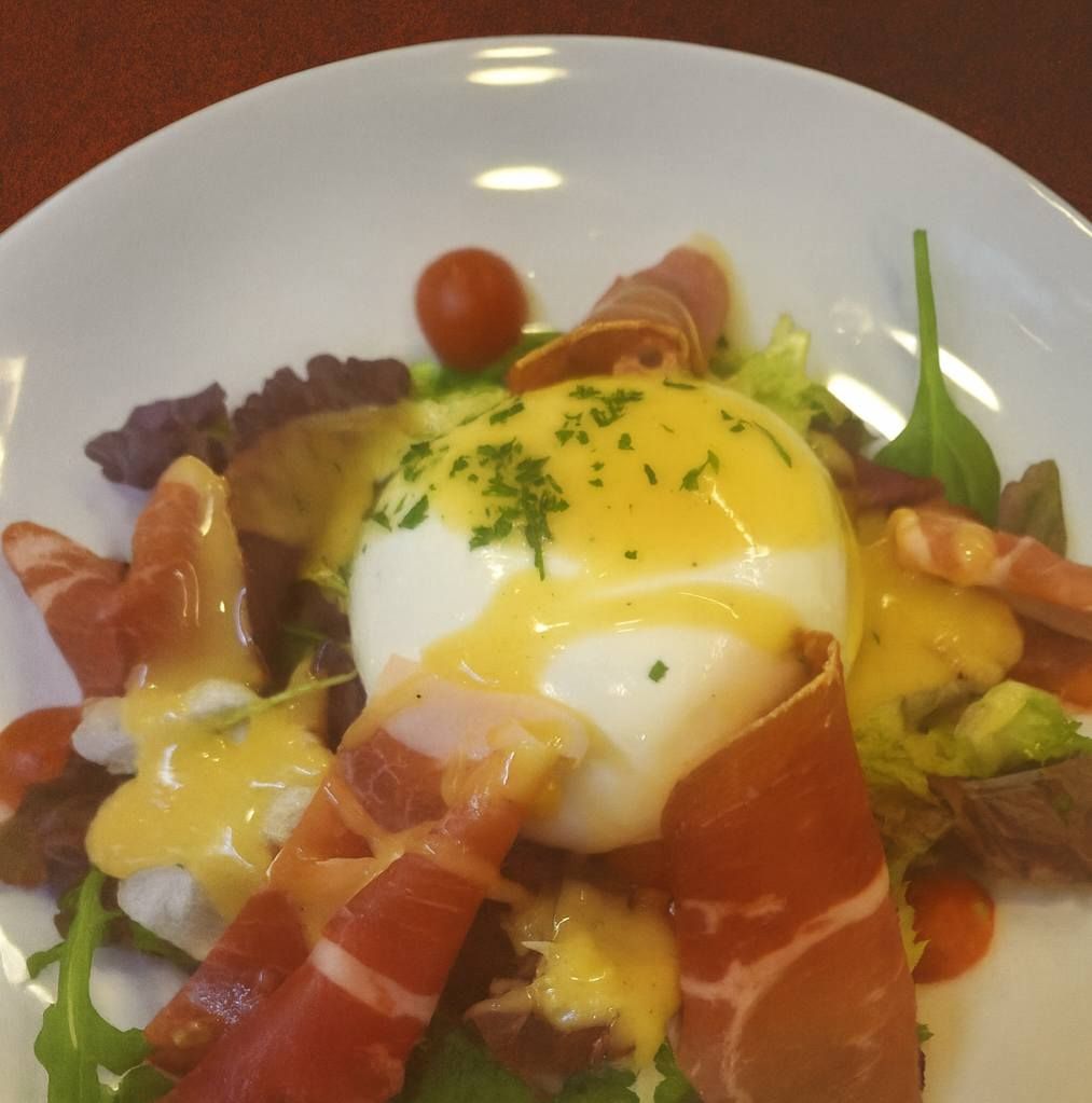 Huevo escalfado con salsa holandesa, prosciutto y verduras en un plato blanco.
