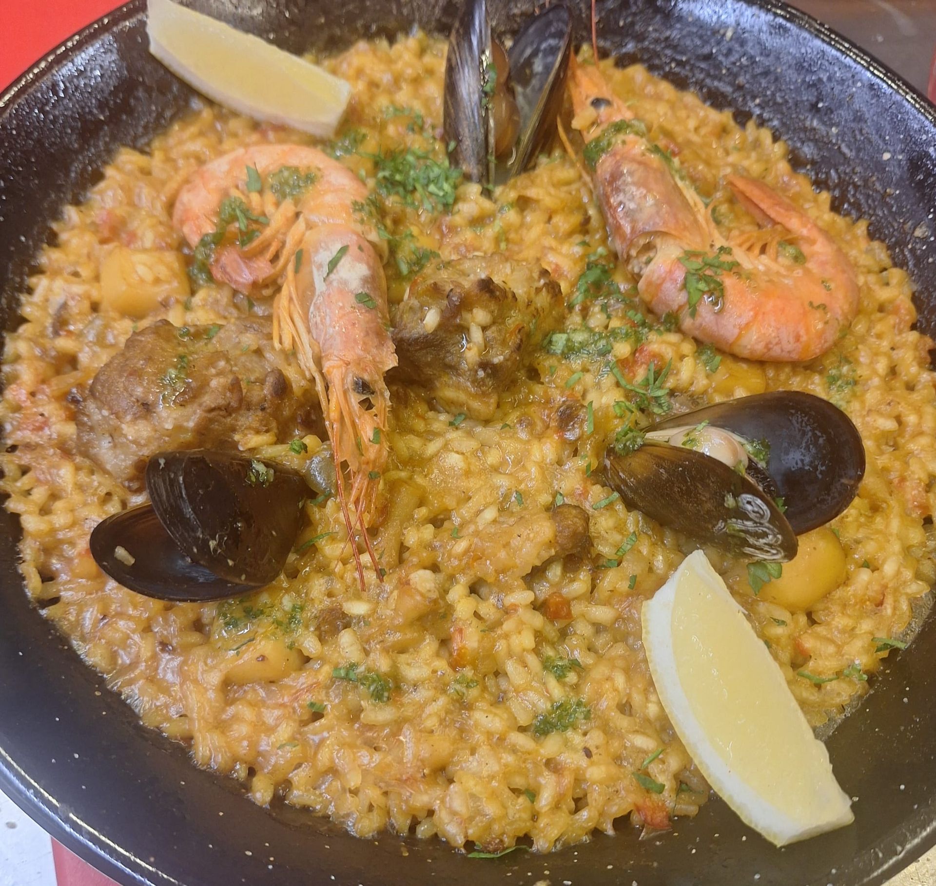 Paella con marisco, gajos de limón en sartén redonda y negra.