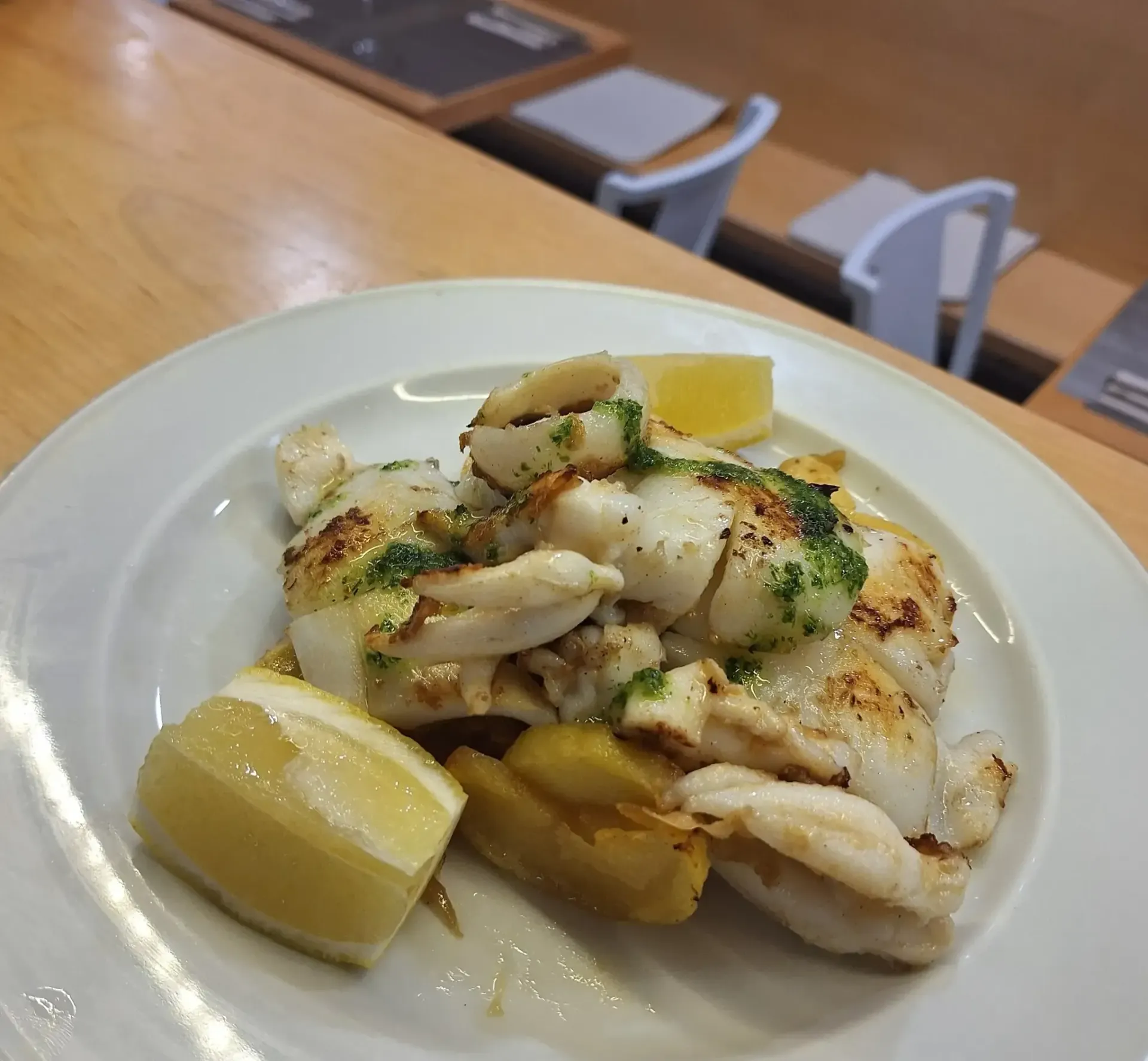 Pescado a la parrilla en plato blanco con rodajas de limón.