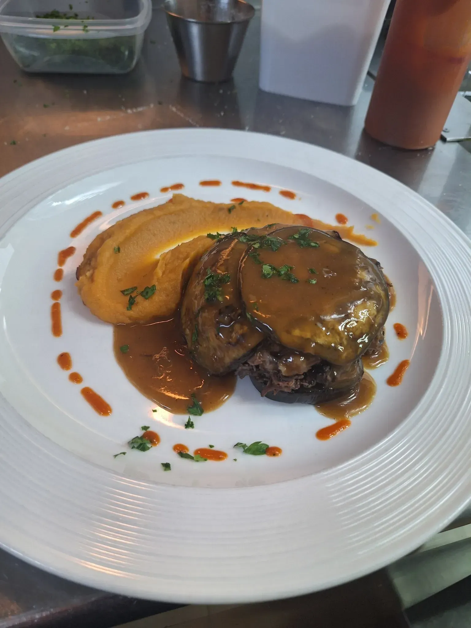 Bistec con salsa y puré de batata en un plato blanco, rociado con salsa y perejil.