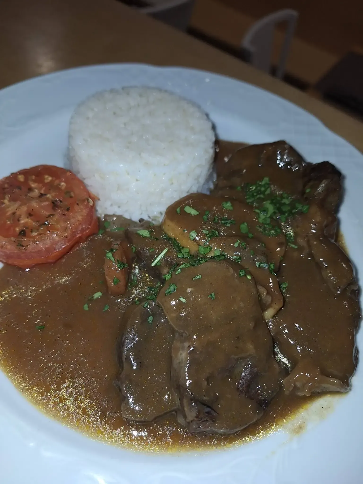 Plato de comida: carne estofada con salsa, arroz y rodaja de tomate.