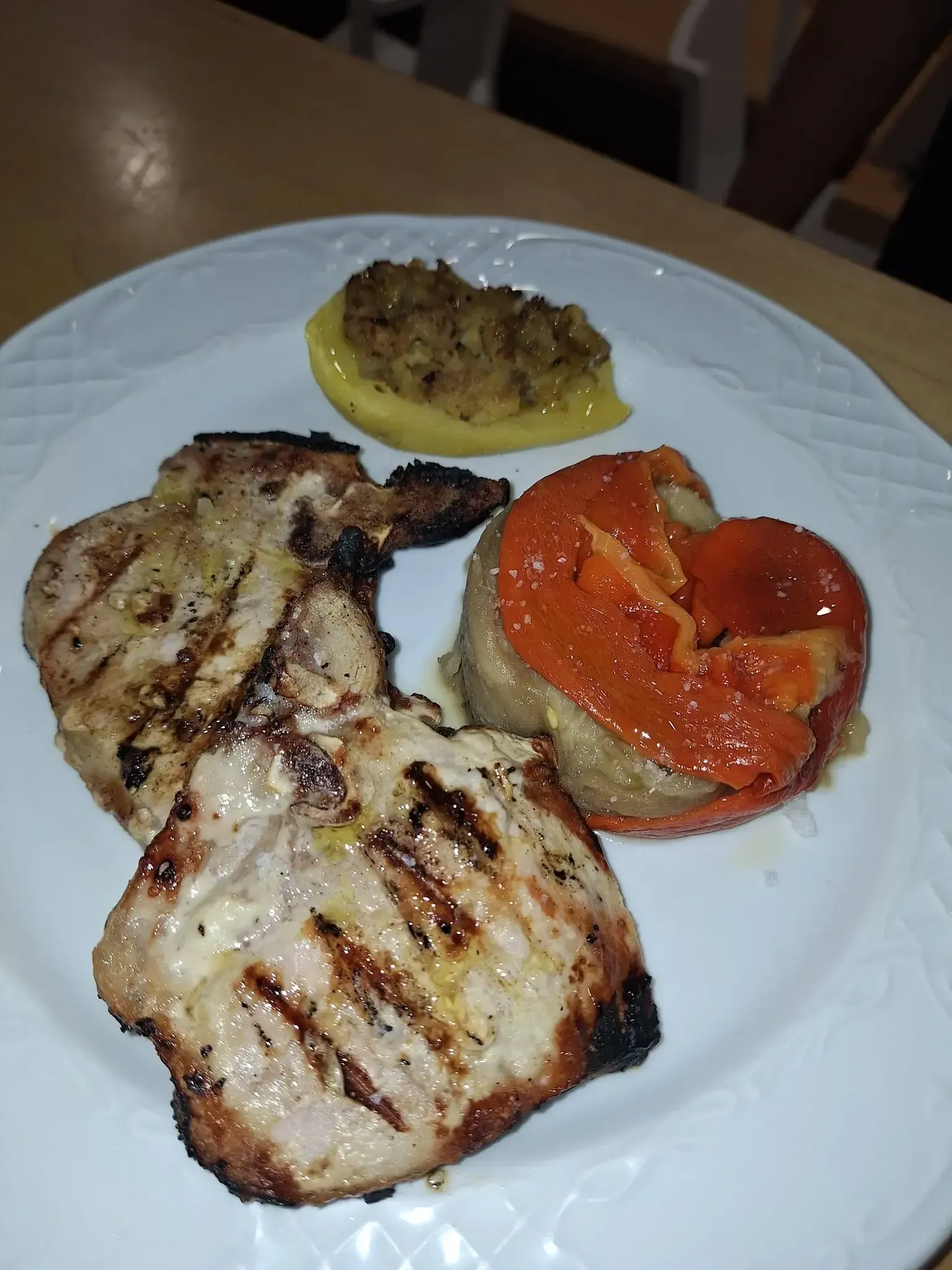 Chuletas de cerdo a la parrilla, pimiento asado y calabacín en un plato blanco.