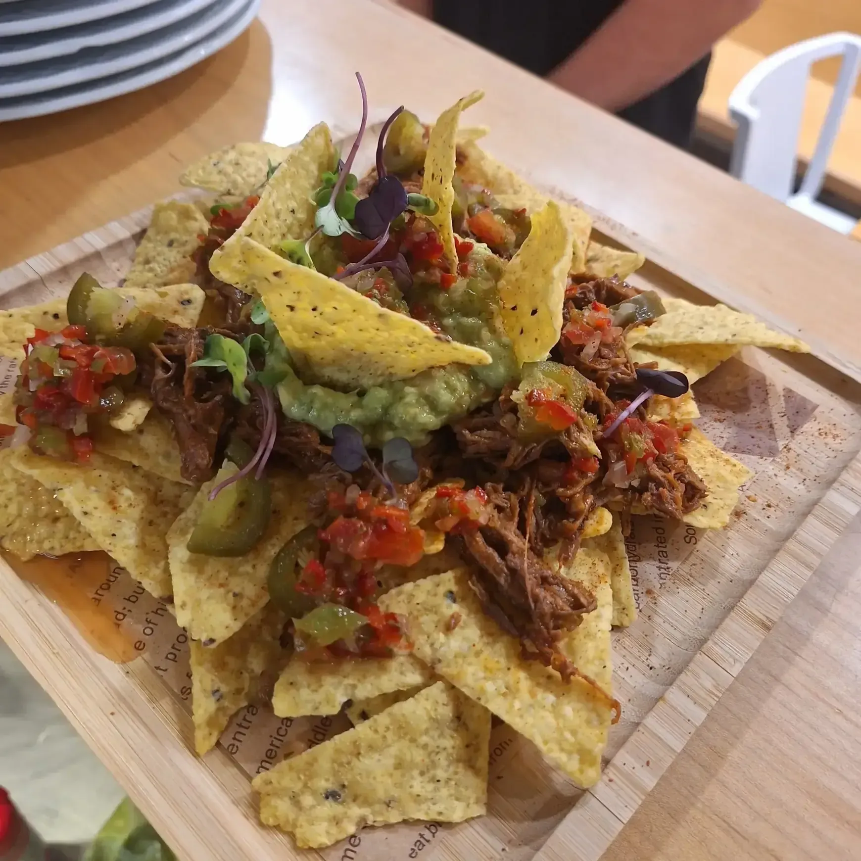 Nachos en bandeja de madera, cubiertos con guacamole, salsa y carne desmenuzada.