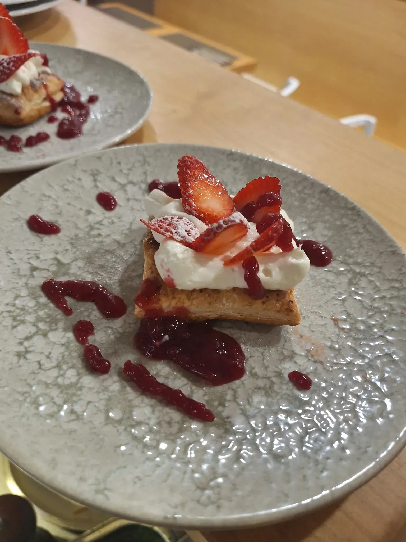 Postre de tarta de fresas sobre un plato gris moteado, con salsa roja y fresas frescas.
