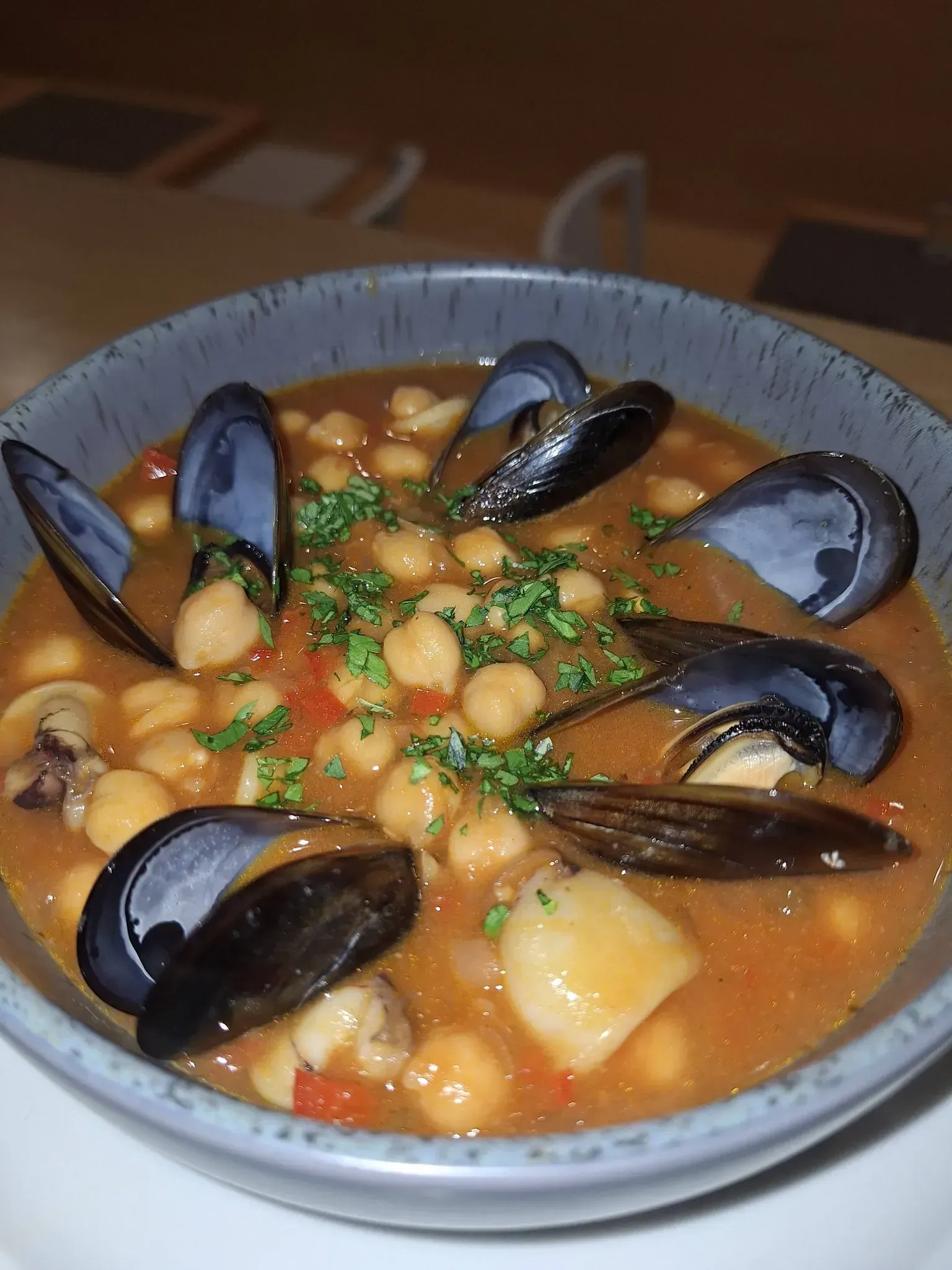 Cuenco de guiso de mejillones y garbanzos, con caldo de naranja, adornado con perejil.