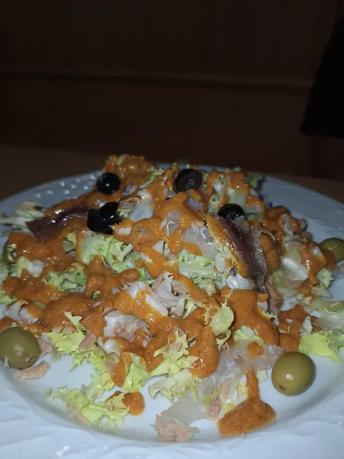 Ensalada en plato, lechuga, anchoas, aceitunas y salsa rojiza.