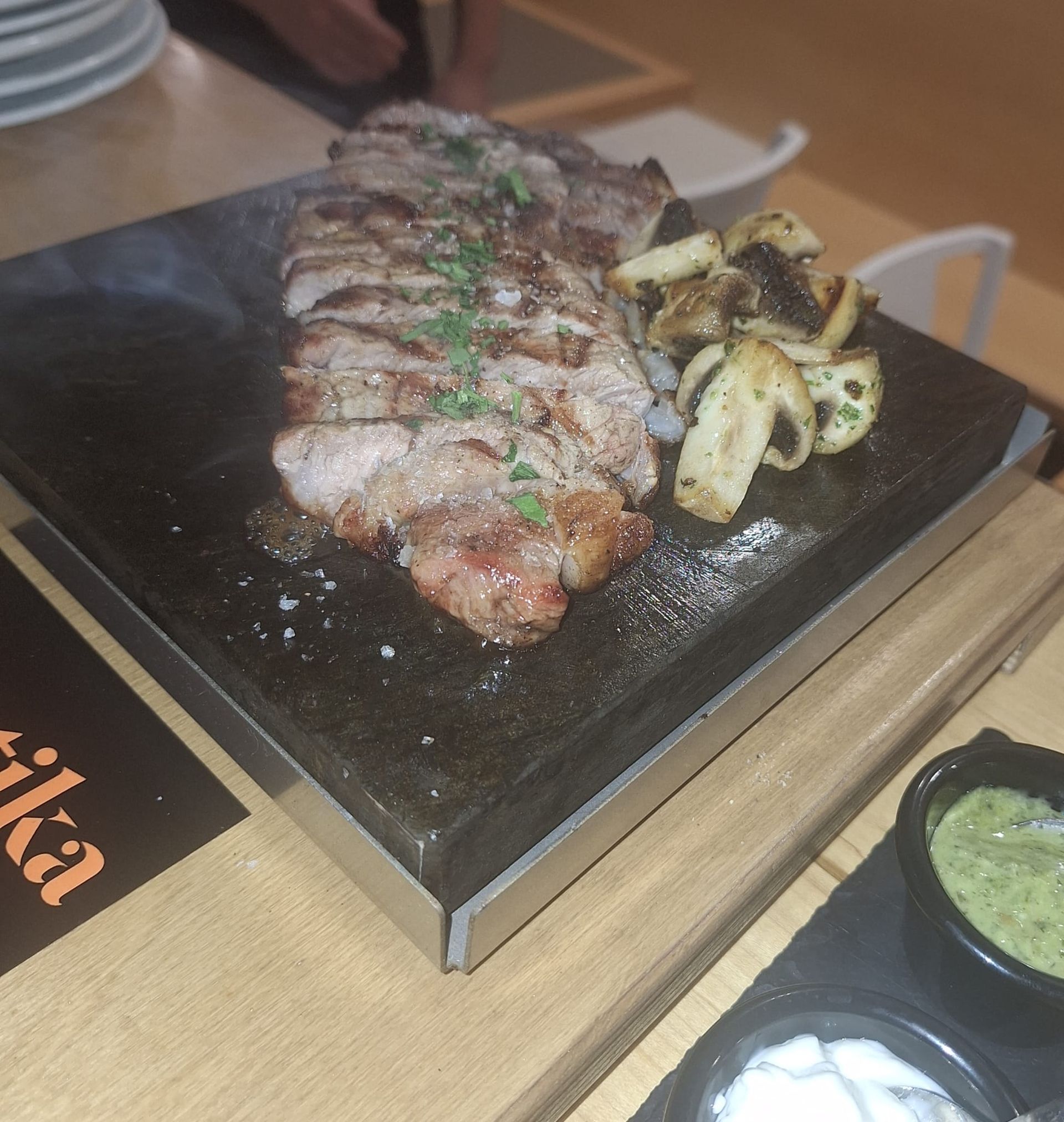 Fideuá con mejillones en un plato blanco. Al fondo, una persona y un plato pequeño con salsa.