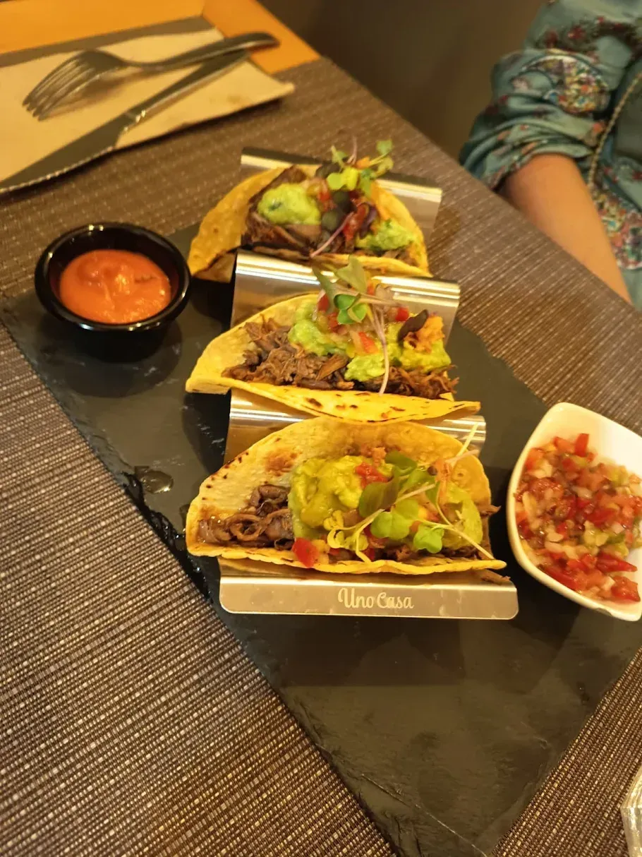 Tacos en plato de pizarra, servidos con salsa y salsa.