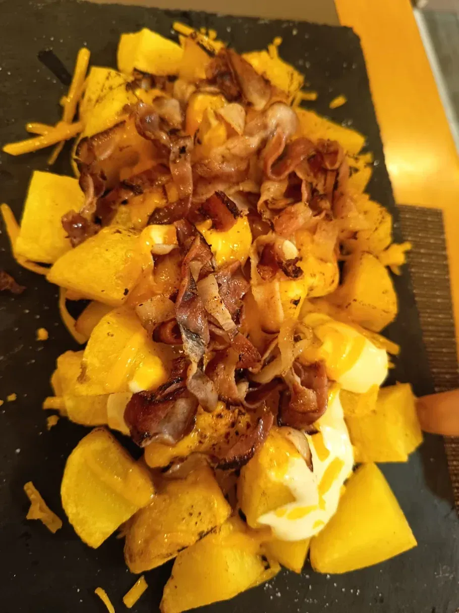 Patatas asadas con cebollas caramelizadas y salsa en un plato negro.