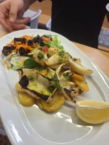 Calamares a la plancha con patatas, ensalada y limón en un plato ovalado blanco.