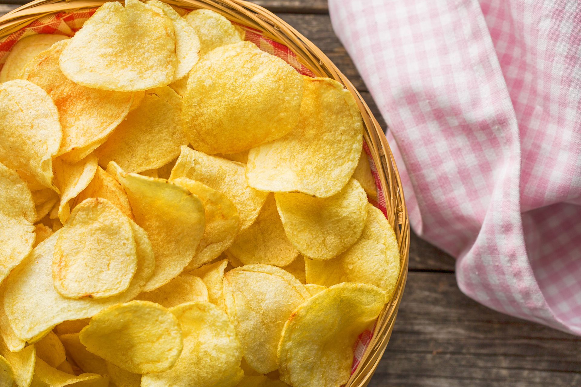 Papas fritas en una canasta tejida con un mantel a cuadros rosa y blanco sobre una mesa de madera.