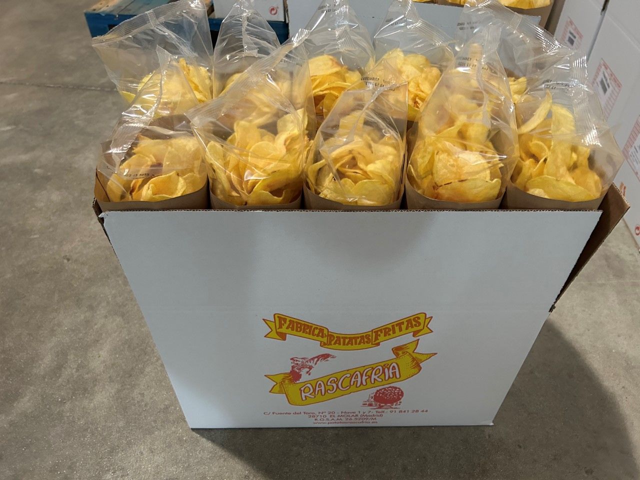 Caja de patatas fritas en bolsas de plástico transparente, con patatas amarillas visibles.