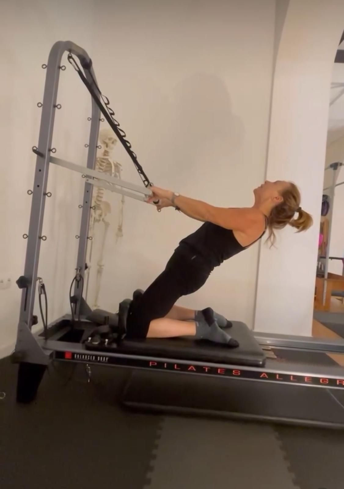 Una mujer con una camisa roja está haciendo una pose de yoga en una máquina de pilates.