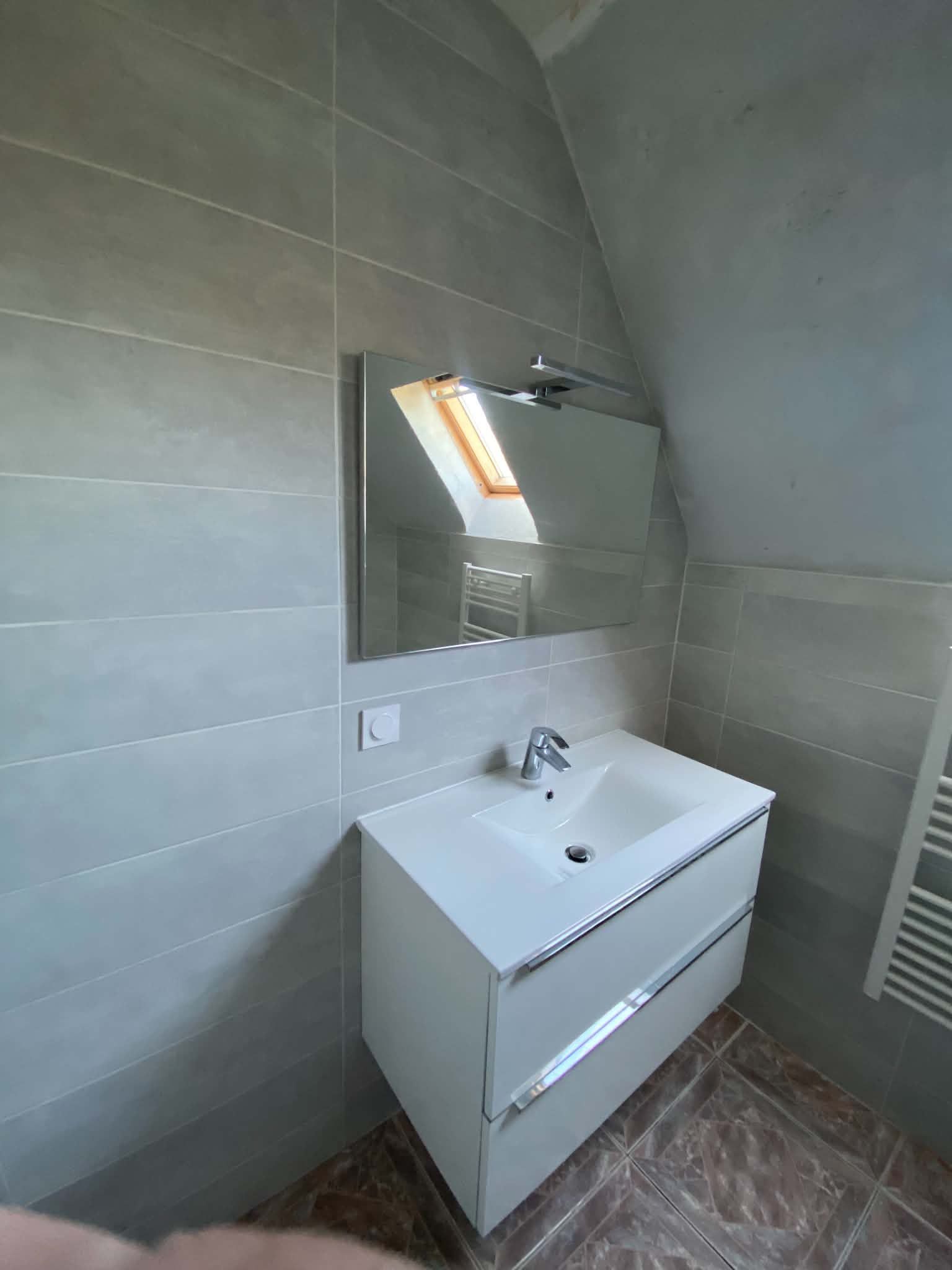 Meuble-lavabo moderne avec lavabo, miroir et puits de lumière au-dessus, sur fond de murs carrelés.