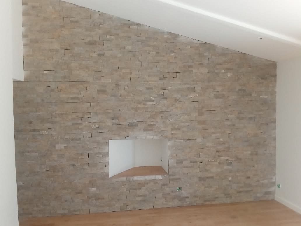 Salon avec un mur en pierre et une petite cheminée encastrée.