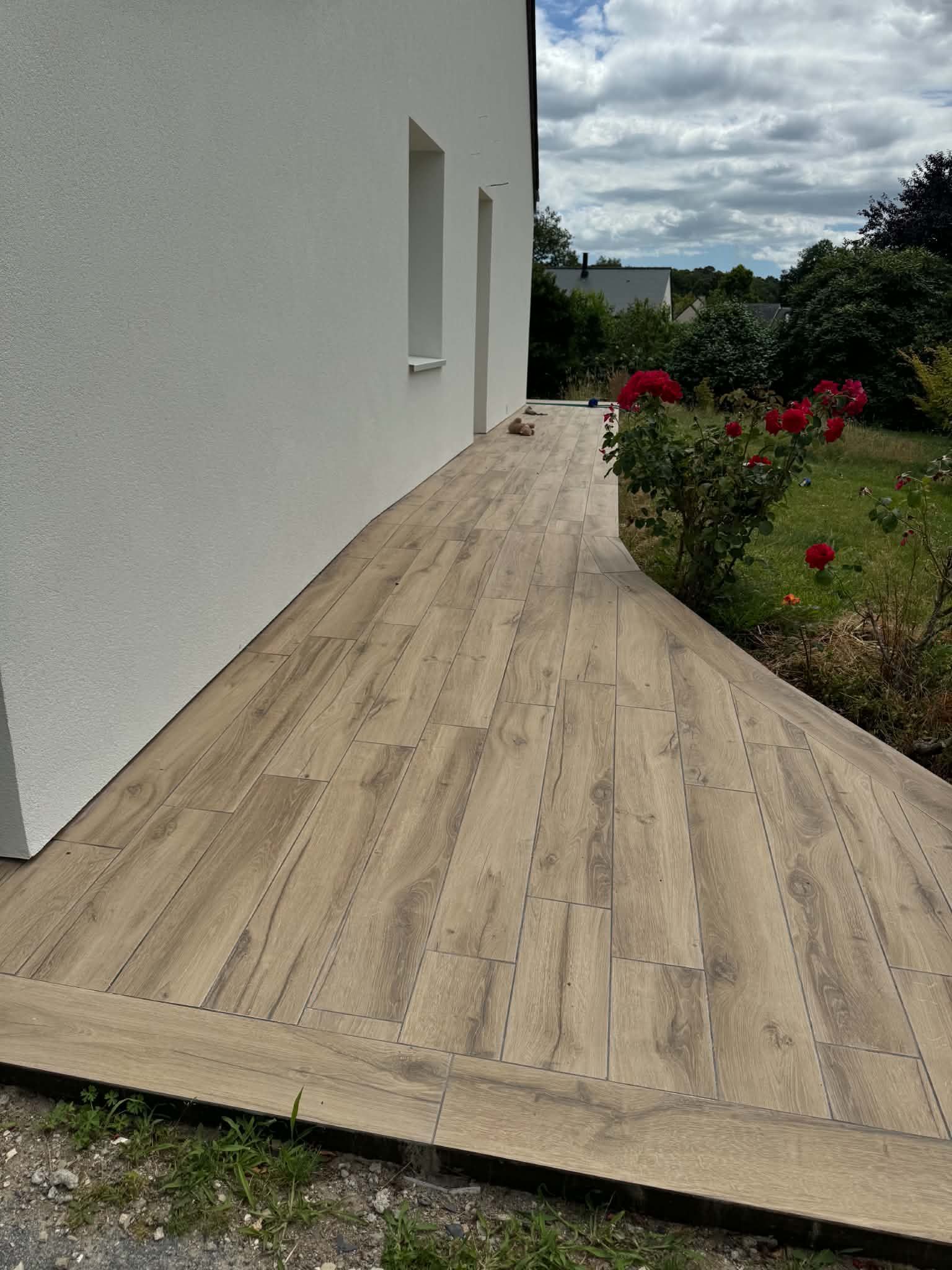 Terrasse en bois jouxtant une maison, bordée d'un jardin aux fleurs.