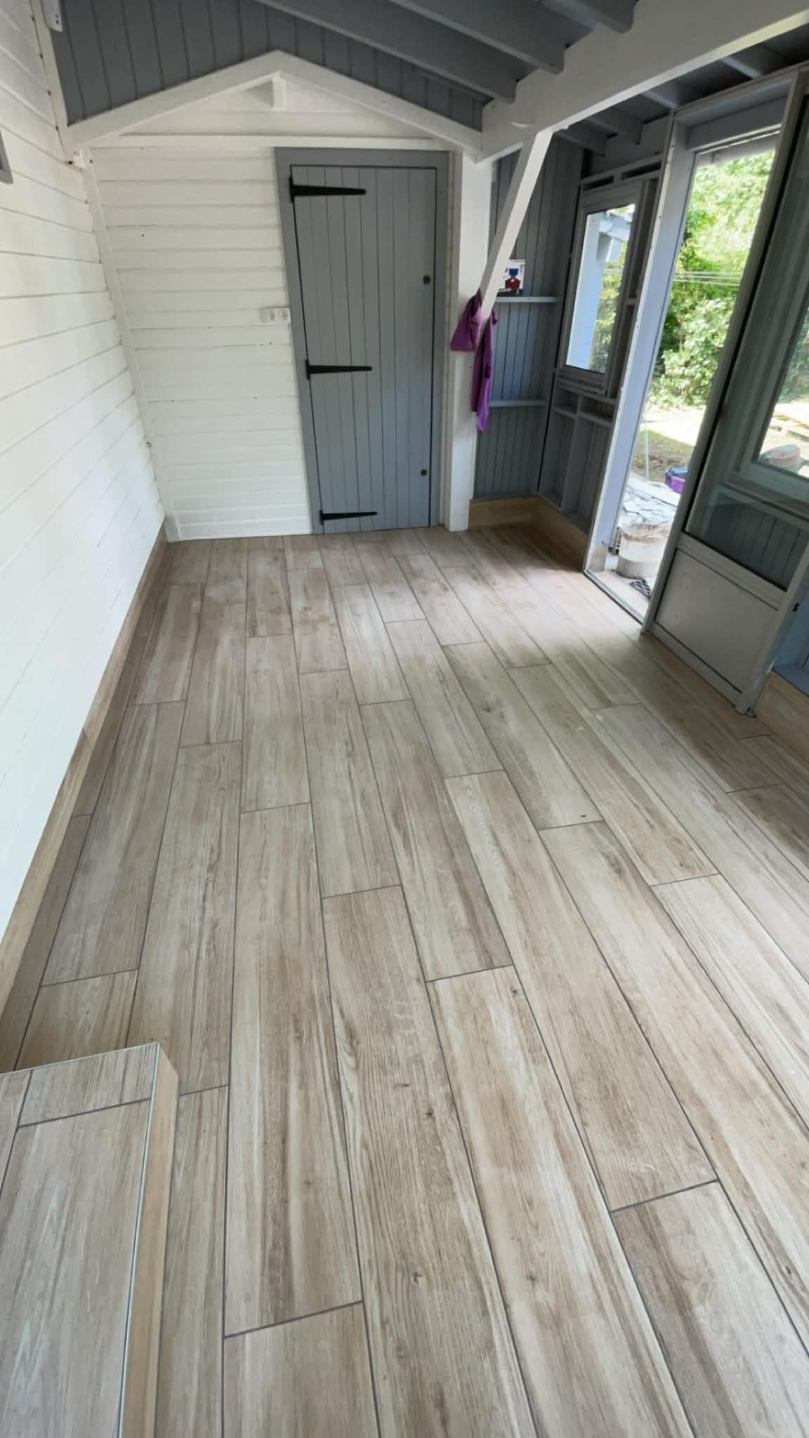 Véranda couverte vide avec parquet, porte et fenêtres sur la droite.