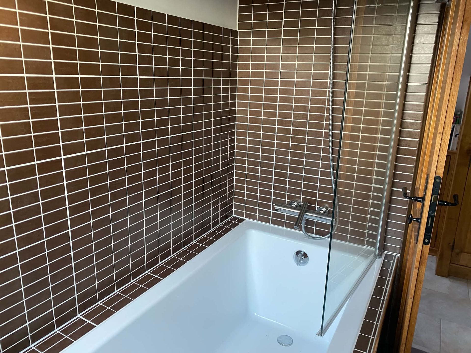 Salle de bains moderne avec douche carrelée et baignoire derrière une paroi de verre.