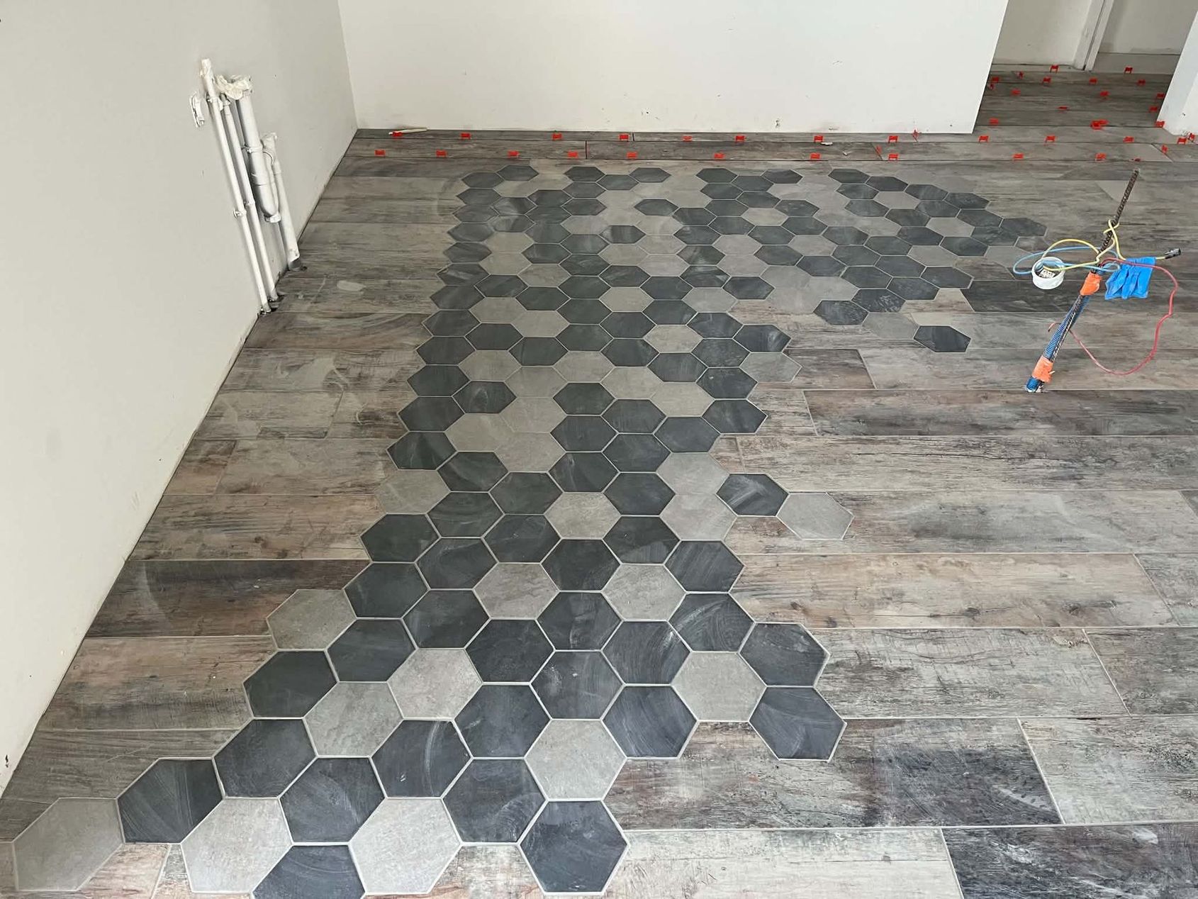 Sol partiellement carrelé avec des carreaux hexagonaux sur des lames dans une pièce non finie.