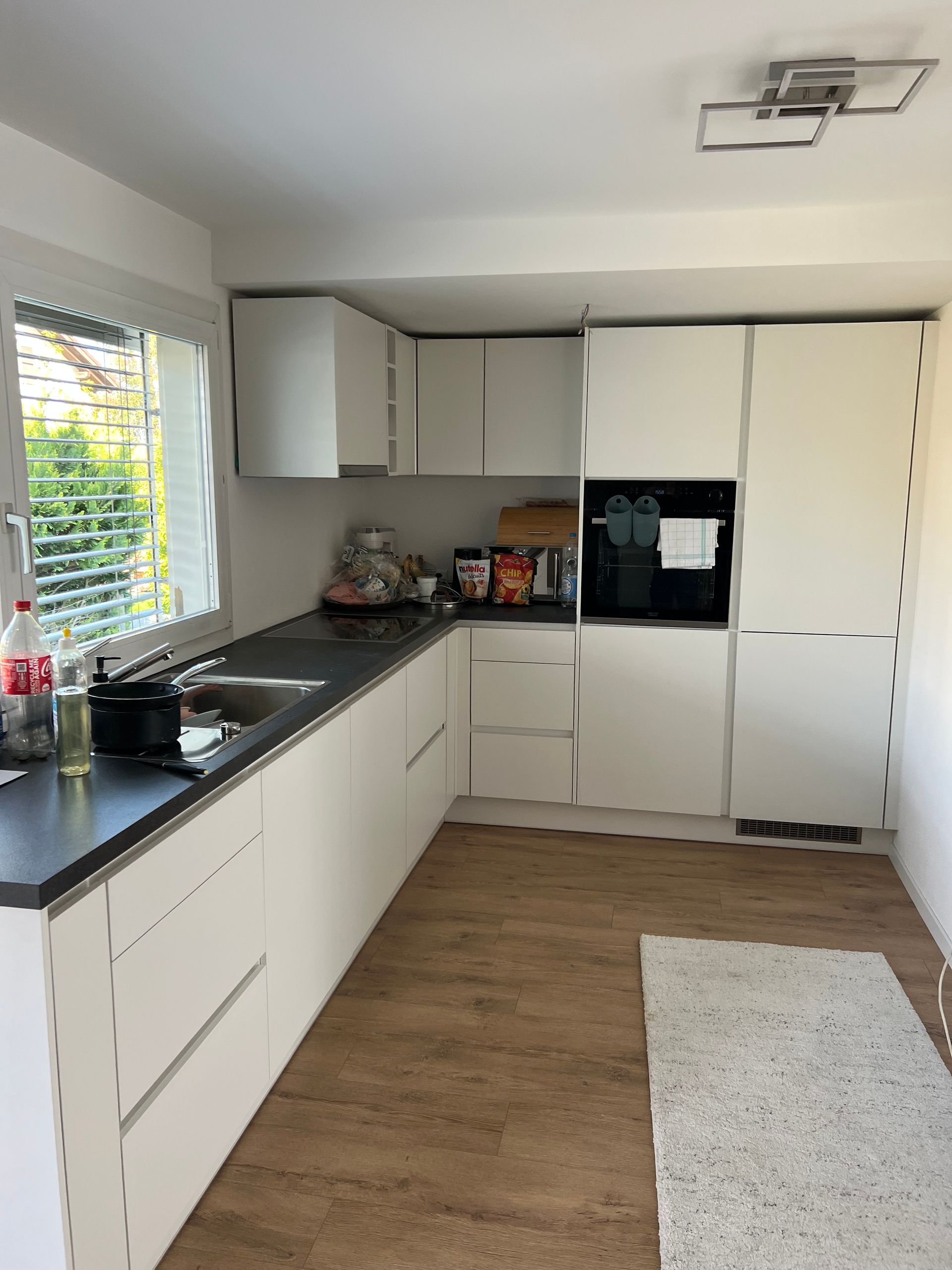 Moderne weiße Küche mit dunkler Arbeitsplatte, Edelstahlspüle und Holzbodenoptik.