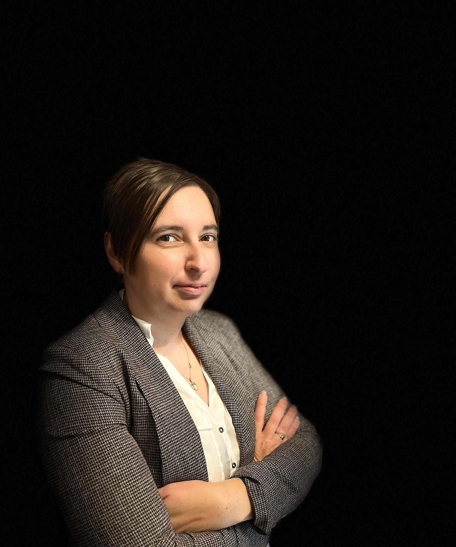 Personne aux bras croisés portant une veste grise sur fond noir.