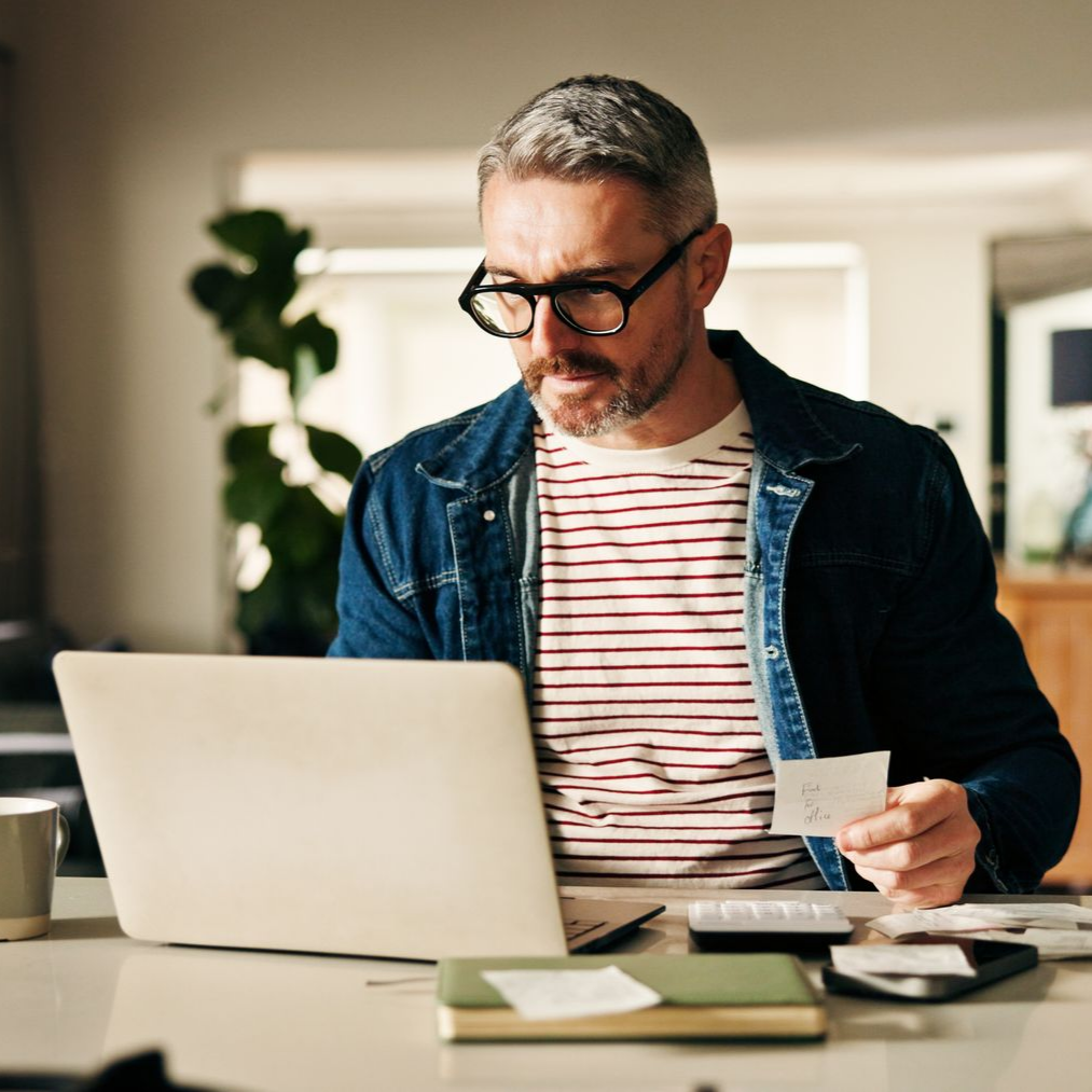 Un homme travaille sur un ordinateur portable à un bureau, tenant une carte dans un bureau à domicile.