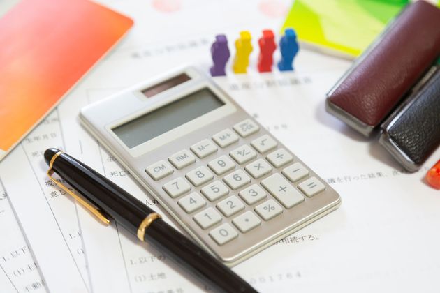 Calculatrice, stylo et papier sur un bureau avec des post-it colorés et des trombones.
