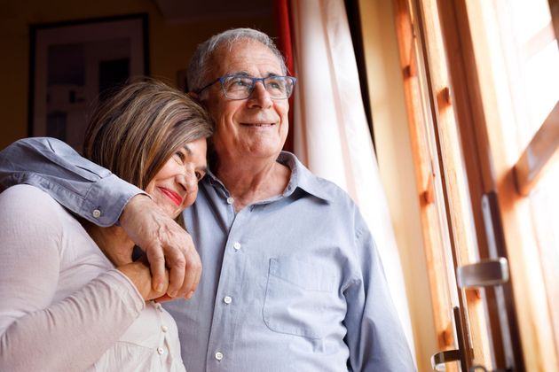 Deux personnes sourient près d'une fenêtre ensoleillée, l'une passant un bras autour de l'autre.