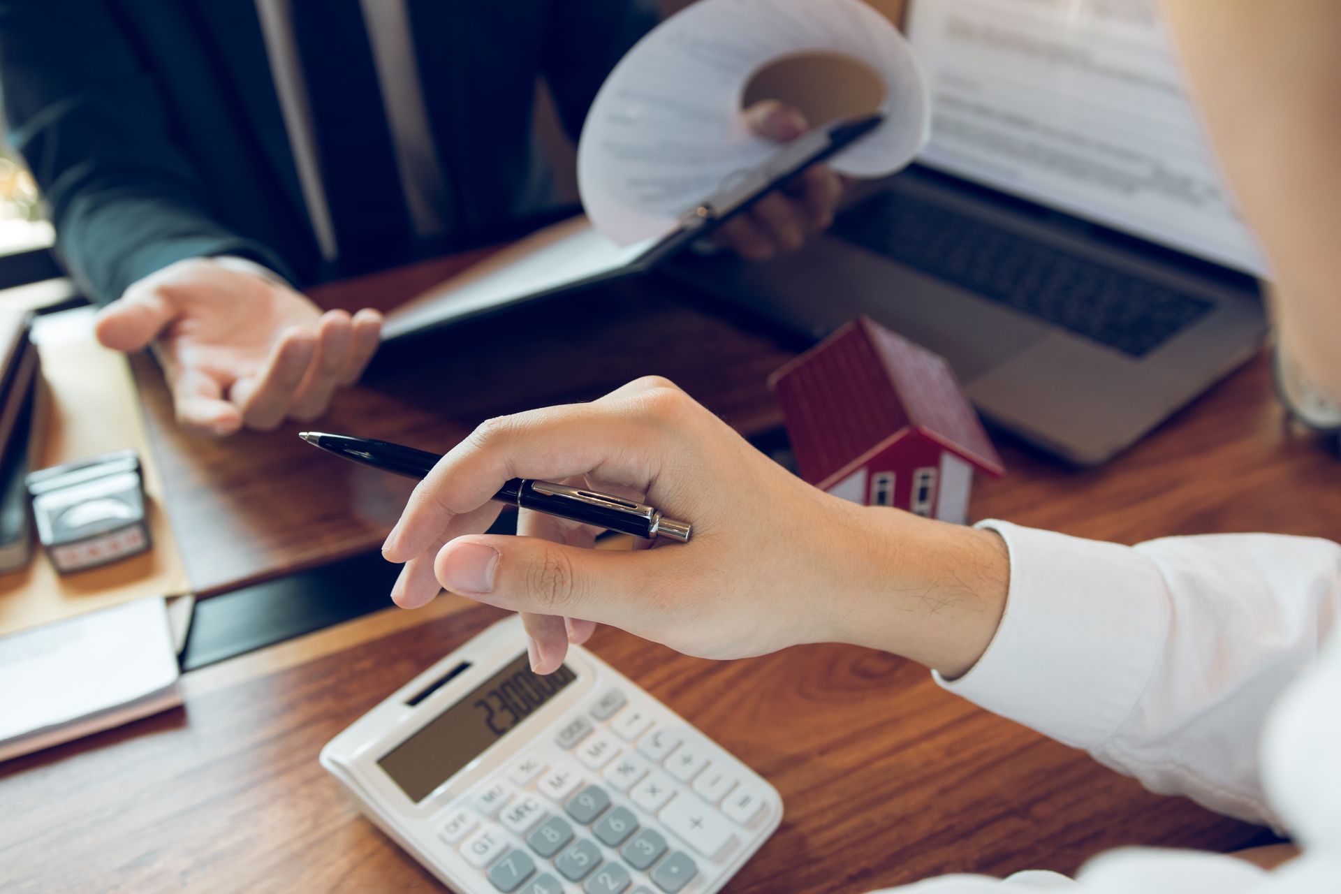 Des mains utilisent une calculatrice et un stylo lors d'une analyse financière à un bureau où se trouvent des documents et un ordinateur portable.
