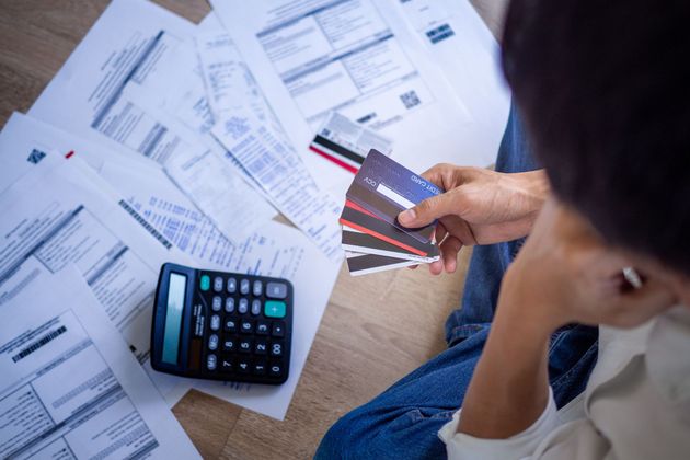 Une personne vérifie ses factures et ses cartes de crédit à côté d'une calculatrice posée sur une table.