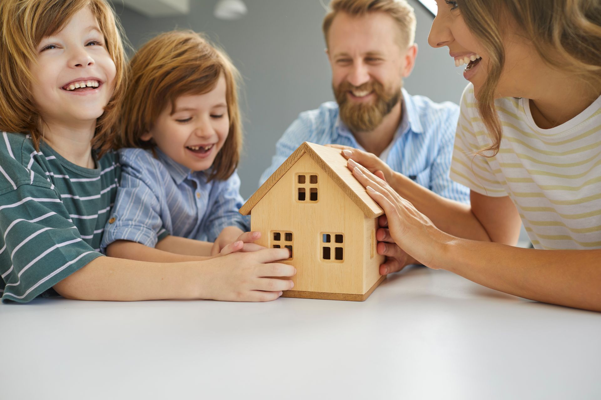 Une famille réunie autour d'une petite maquette de maison en bois.