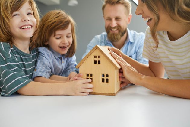 Une famille réunie autour d'une petite maquette de maison en bois.