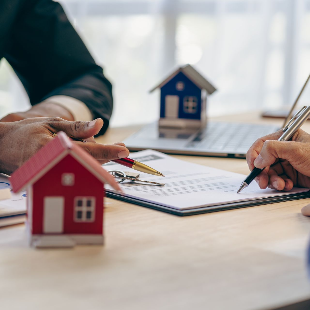 Des mains échangent des clés au-dessus d'un contrat immobilier, des maisons témoins étant disposées sur une table.