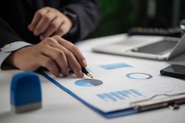 Des mains marquent des graphiques sur un bloc-notes à côté d'un ordinateur portable dans un environnement de bureau.