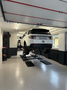 Ein Mechaniker balanciert einen Reifen auf einer Maschine in einer Werkstatt aus. Der Mechaniker trägt einen blauen Overall.