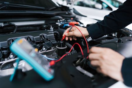 Mechaniker verwendet ein Multimeter zur Diagnose eines Automotors in einer Werkstatt.