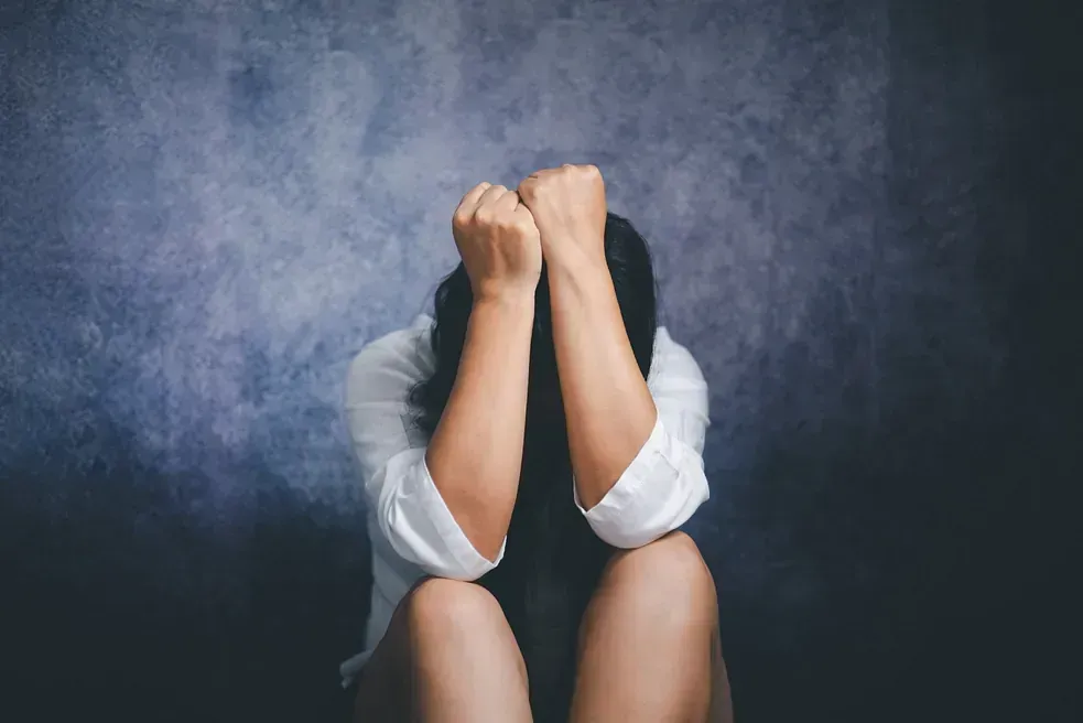 Una mujer está sentada con la cabeza entre las manos.