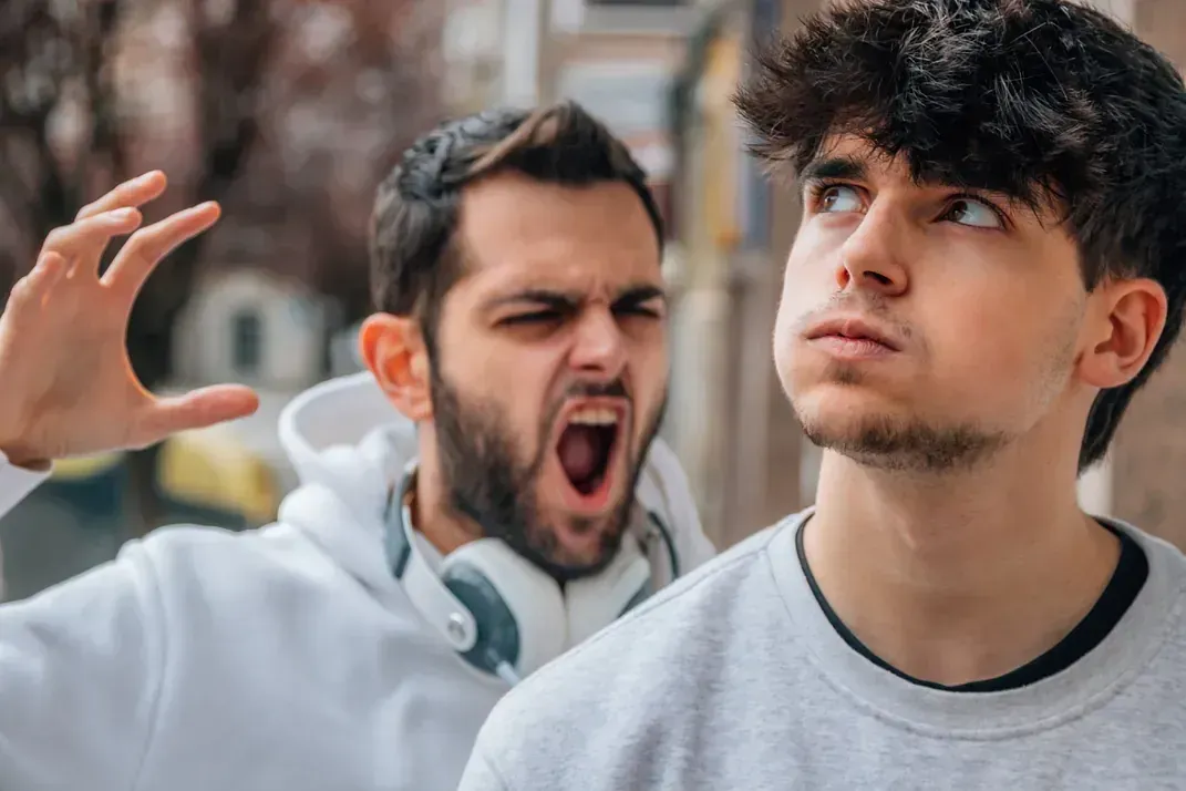 Dos jóvenes están parados uno al lado del otro y uno de ellos le está gritando al otro.